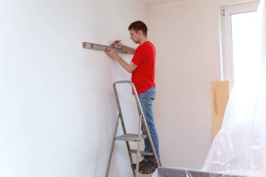 Kabarcık seviyesindeki aletle duvarın seviyesini kontrol eden tamirci. Yenileme konsepti