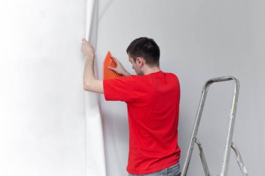 Duvara duvar kağıdı yapıştıran genç profesyonel bir tamirci. Apartman onarımı. Ev yenileme konsepti.