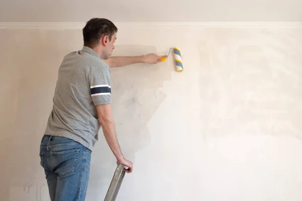 Een man die de muur met een roller klaarmaakt. Reparatie van het interieur. Jonge mannelijke decorateur schildert een muur in de lege kamer. Concept renovatie doe het zelf. — Stockfoto