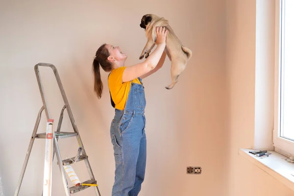 Mujer feliz hace reparaciones en su apartamento con su perro pug divertido. felicidad en previsión de un nuevo hogar y movimiento. vida independiente con una mascota. — Foto de Stock