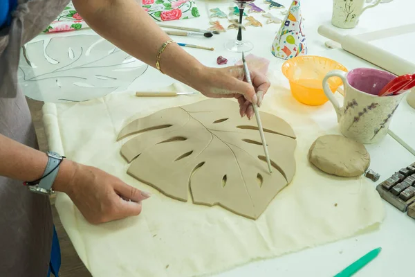 Woman hand potter making clay monstera leaf in pottery workshop studio. Process of creating ceramic vase. Handmade, hobby art and handicraft concept — Stock Photo, Image