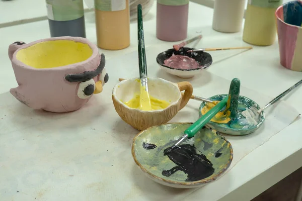 Дитяча дівчина малює пензлем на глиняній керамічній чашці в студії кераміки. Розвиток мистецтва і живопису у дітей — стокове фото