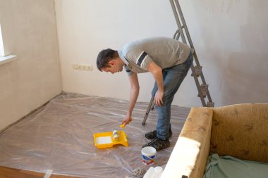 Duvarı silindirle kaplayan bir adam. İçerisinin tamiri. Genç erkek dekoratör evde bir duvar boyuyor. Yenileme işini kendin yap.