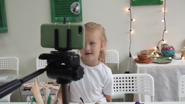 粘土をモデリングしてビデオを記録し スマートフォンのカメラのために話す女の子Vlogger 子供のための興味深いコンテンツを作成するセラミックスタジオでのキッドブロガー — ストック動画