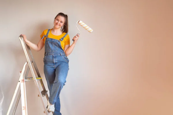 La mujer feliz hace reparaciones en su apartamento. Divertida hembra con un rodillo en escalera con espacio para copiar. Independiente mujer soltera. — Foto de Stock
