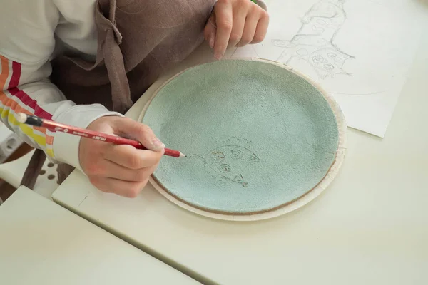 Kid hand painting with pencil on colored clay pottery cup in ceramic workshop studio. Development of art and painting in children. Close-up. — Stock Photo, Image