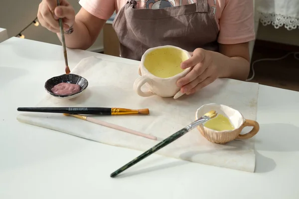 Kind meisje schilderen met borstel op klei aardewerk beker in keramische atelier. Ontwikkeling van kunst en schilderkunst bij kinderen — Stockfoto