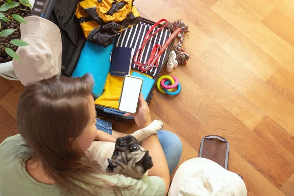 Wanita pengepakan bagasi untuk liburan dengan anjing pug. Gadis mempelajari aturan untuk mengangkut hewan peliharaan untuk bepergian. — Stok Foto