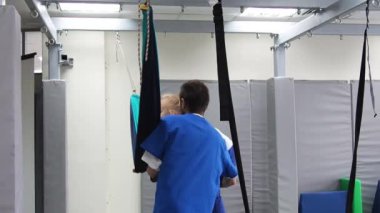 Duyusal entegrasyon sırasında salıncakta sallanan fizyoterapist kız çocuğu. Çocuklarda vestibüler aygıtın geliştirme işlevleri.
