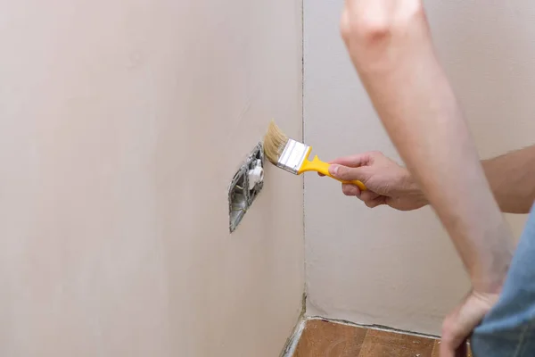 Man priming de muur met een borstel in de buurt van socket. Reparatie van het interieur. Jonge mannelijke decorateur schilderen een muur in de lege kamer — Stockfoto
