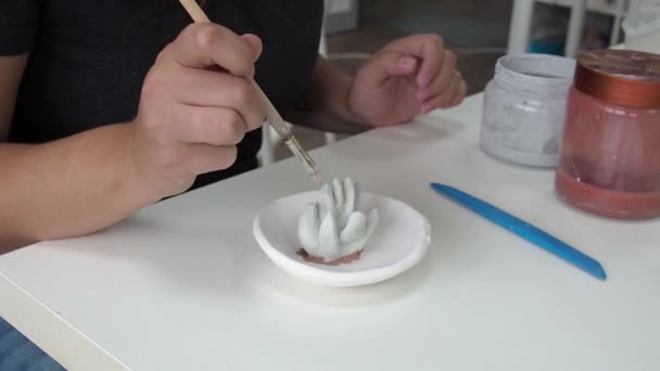 Поттер наносит глазурь кистью на глиняную тарелку для украшений. Женщина применяет глазурь первого уровня на своем произведении искусства — стоковое видео