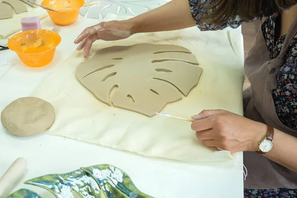 Woman hand potter making clay monstera leaf in pottery workshop studio. Process of creating ceramic vase. Handmade, hobby art and handicraft concept — Stock Photo, Image