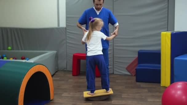 Ragazza con terapeuta fare esercizio sull'equilibrio durante la sessione di integrazione sensoriale. Sviluppo dell'apparato vestibolare e sensazione del corpo nello spazio. — Video Stock