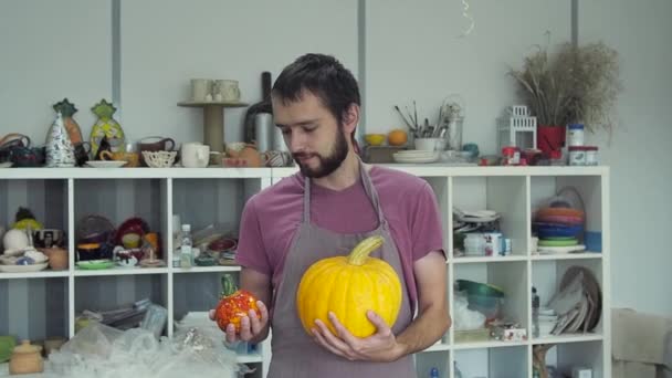 Man vergelijken plantaardige pompoen en keramische pompoen in aardewerk studio. Halloween kunstsymbool. — Stockvideo