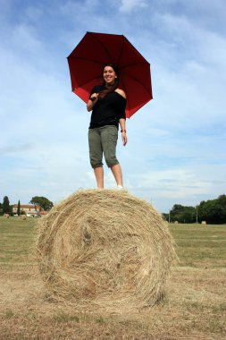 Yazın Toskana 'da saban tarlasında saman topunda şemsiyenin altında güneşin tadını çıkaran genç bir kadın.