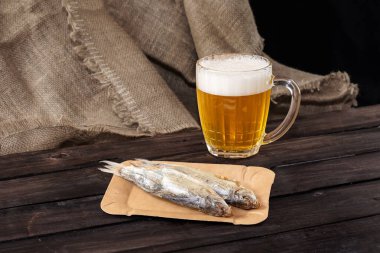 Koyu arkaplanda kurutulmuş balık olan bir kupa bira.