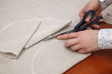 Kadının elleri terzi makası ile kumaş kesiyor.