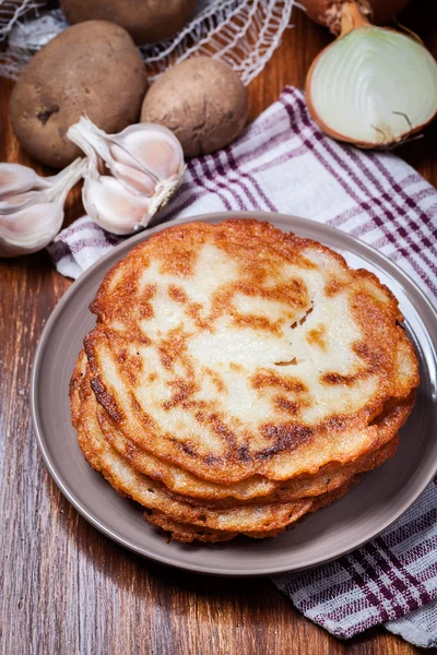 Stack of potato pancakes on a wooden table. In the background po — Stock Photo, Image