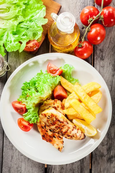 Grilled chicken breasts served with fries and fresh salad — Stock Photo, Image