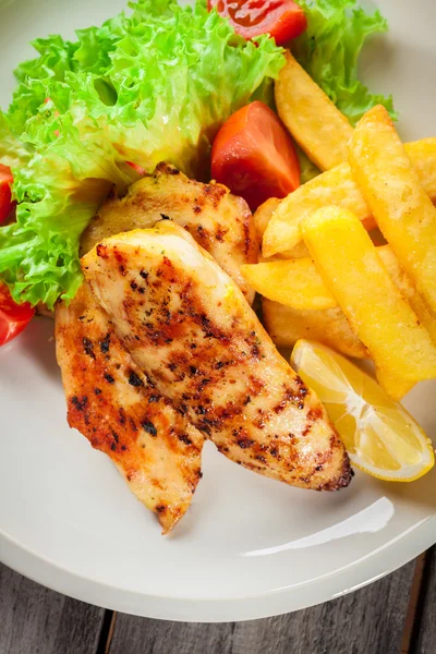 Grilled chicken breasts served with fries and fresh salad — Stock Photo, Image