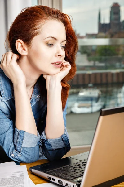 Jeune femme d'affaires rousse ou étudiante travaillant avec des documents et un ordinateur portable près de la fenêtre — Photo