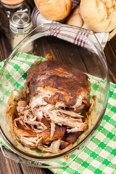 Slow cooked pulled pork shoulder with onion and garlic in casserole dish