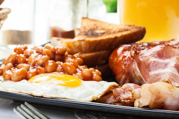 Petit déjeuner anglais complet avec bacon, saucisse, œuf, haricots cuits au four et jus d'orange — Photo