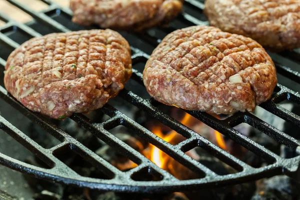 Raw burgers on barbecue grill with fire — Stock Photo, Image