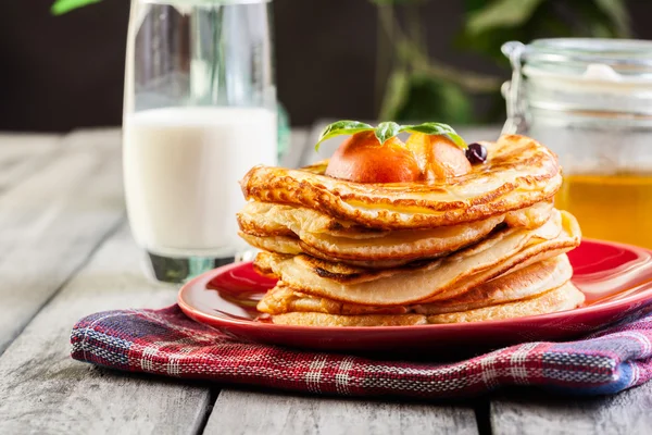 Pancakes with honey, fruit and glass of milk — Stock Photo, Image