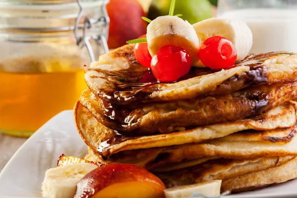 Pancakes with chocolate sauce fruit and glass of milk — Stock Photo, Image