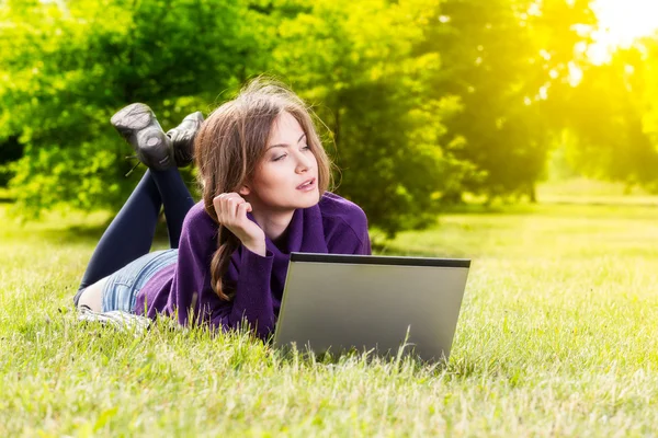 Jovem mulher usando laptop no parque deitado na grama — Fotografia de Stock