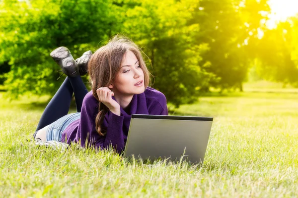 Young woman using laptop in the park lying on the grass — Stock Photo, Image