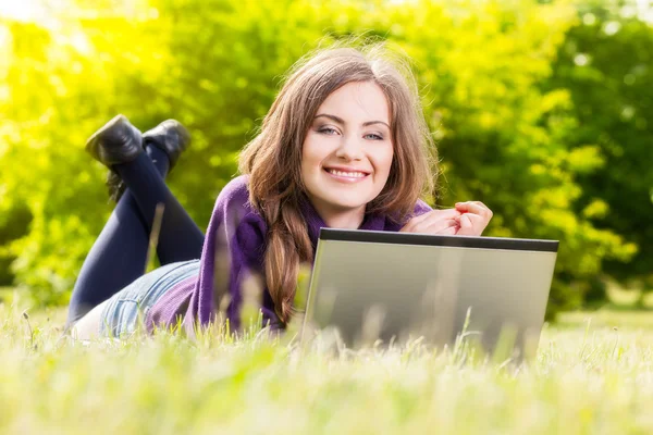 Jonge vrouw met laptop in het park liggen op het gras — Stockfoto