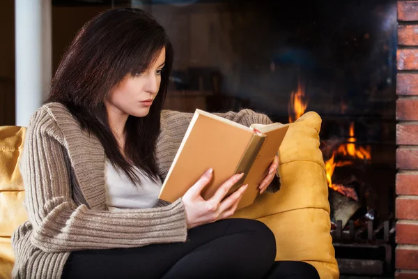 Mujer leyendo un libro junto a la chimenea — Foto de Stock