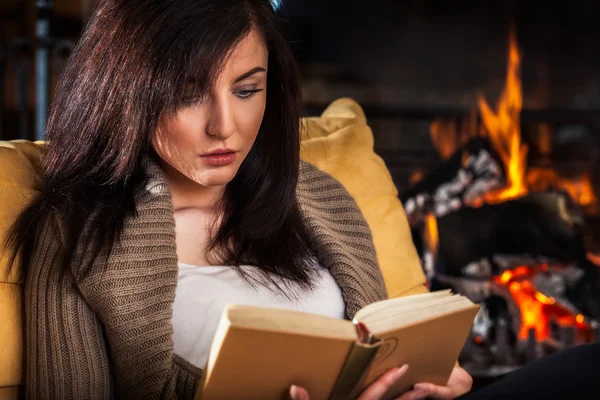 Mujer leyendo un libro junto a la chimenea — Foto de Stock