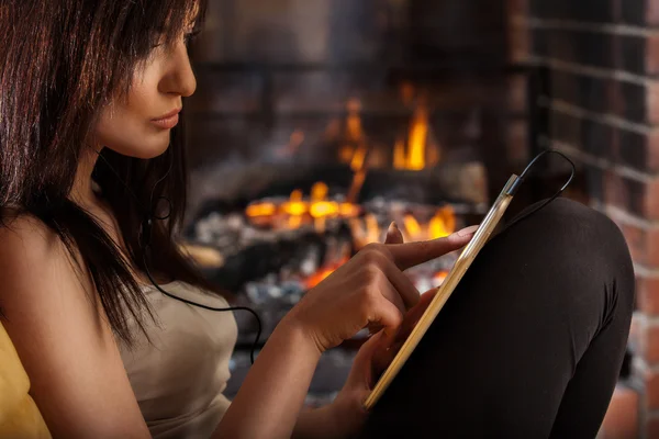 Mujer usando tableta digital sentada junto a la chimenea —  Fotos de Stock