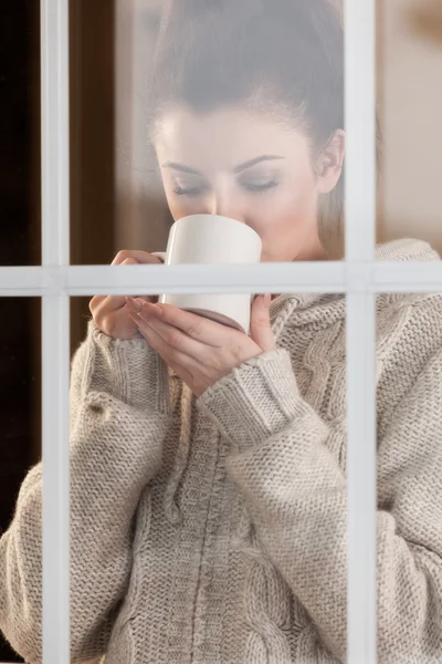 Vrouw drinken warme drank permanente door het venster — Stockfoto