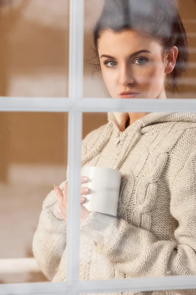 Femme buvant une boisson chaude debout près de la fenêtre — Photo