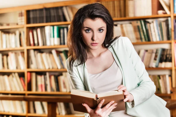 Kvinna läser en bok framför bokhyllor — Stockfoto