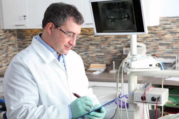 Dentist holding  clipboard and writing — Stock Photo, Image