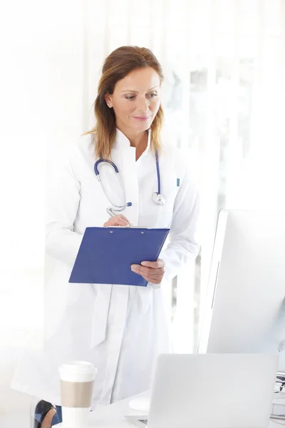 Médico que trabaja en la computadora y la escritura — Foto de Stock