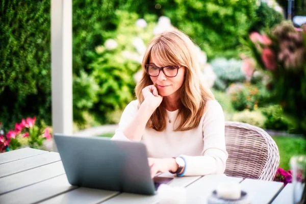 幸せな成熟した女性は庭に家に座って ビデオ通話をしながらノートパソコンを使用して — ストック写真