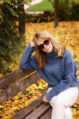 Dışarıdaki bankta dinlenirken derin düşüncelere dalmış orta yaşlı bir kadının portresi. Sonbahar havası.