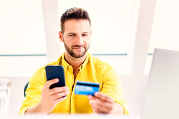Shot of man holding credit card and mobile phone in his hands while paying bills with credit card.