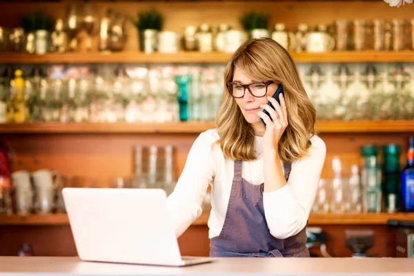 Skott Leende Kvinnliga Servitris Med Hjälp Mobiltelefon Och Bärbar Dator — Stockfoto