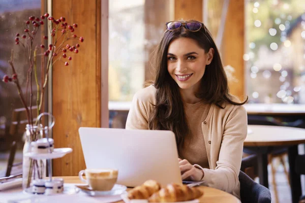 一个漂亮的微笑的女人坐在咖啡店 在笔记本电脑上上网工作的肖像照片 小商业 — 图库照片