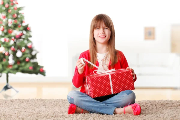 满满一帧快乐的女孩坐在地板上 同时解开圣诞节礼物的盒子 背景是圣诞节树 — 图库照片
