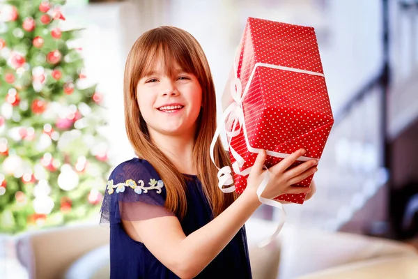Fröhliches Kleines Mädchen Hält Weihnachtsgeschenk Der Hand Während Wohnzimmer Hintergrund — Stockfoto