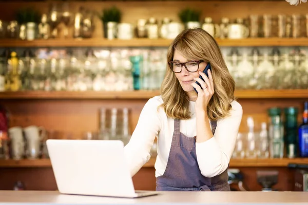 Tiro Garçonete Sorridente Feminino Usando Telefone Celular Laptop Enquanto Estava — Fotografia de Stock