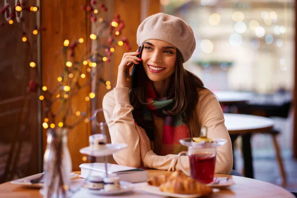 カフェに座っている間に彼女の携帯電話で誰かと話している陽気な笑顔の美しい女性のショット — ストック写真